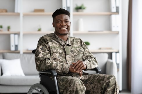 Smiling veteran in military uniform sitting in wheelchair inside an office. 