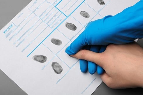 Hand wearing blue rubber glove placing fingerprint of another hand on to visa applicant form with other fingerprints. 