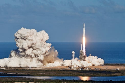 Spaceship launching off ground at Kennedy Space Center with large plume of smoke and ocean surrounding launch pad.   